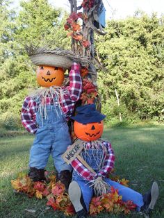 two scarecrows sitting next to each other in front of a tree decorated with pumpkins