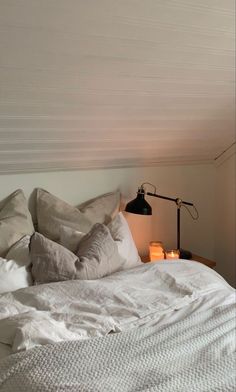 a bed with white linens and pillows in a bedroom next to a wall lamp