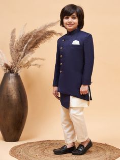 a young boy standing in front of a vase with dried grass on the floor next to it