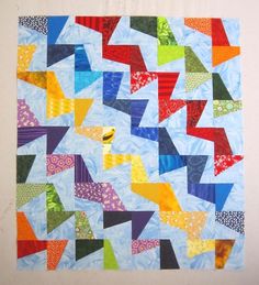 a colorful quilt is hanging on the wall in front of a white wall with a blue background