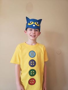 a young boy wearing a t - shirt with buttons on it and a cat hat