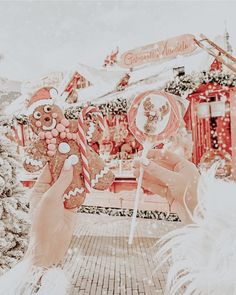 two people holding up candy canes in front of a christmas themed building and trees