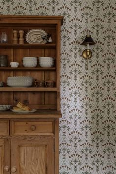 an old wooden china cabinet with dishes on it and wallpaper in the back ground