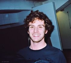 a young man with curly hair smiling at the camera while wearing a black t - shirt