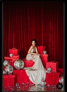 a woman sitting on top of red boxes surrounded by silver balls and confetti