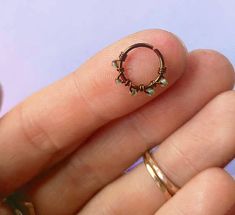 a woman's hand holding a gold ring with green beads