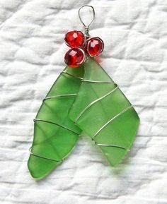 a green leaf with two red beads hanging from it's side on a white surface