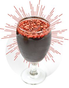 a glass filled with liquid sitting on top of a white table next to a red sprinkle