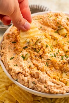 a hand dipping a tortilla chip into a bowl of dip surrounded by chips