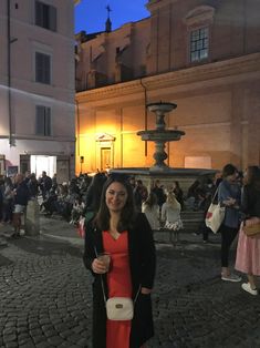 a woman standing in front of a fountain at night with people walking around and onlookers