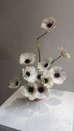 an arrangement of white and black flowers in a vase on top of a marble block