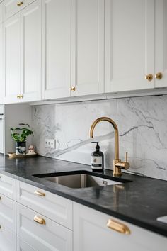 a kitchen with marble counter tops and gold faucets on the sink, along with white cabinets