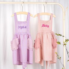 two children's dresses hanging on a clothes rack, one with personalized letters and the other with gingham