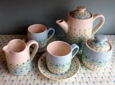 a tea set with matching cups and saucers is on a tablecloth covered table