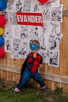 a young boy wearing a spiderman mask standing in front of a wooden fence with balloons