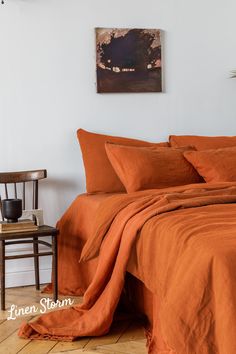 an orange bed spread and pillows in a white room with a chair next to it