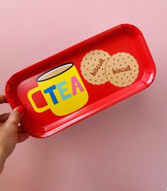 a person holding a red tray with cookies on it and a cup of tea in the middle