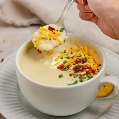 a person holding a spoon full of soup with cheese and crackers on the side