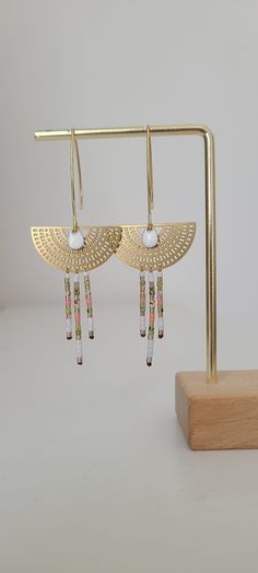 Our beautiful boho chic gold dangling earrings are handwoven with Miyuki beads in shades of white, green, coral and gold. They are mounted on pretty golden half circles and feature a white enameled drop pendant. The ear hooks are made of stainless steel These earrings offer a harmonious blend of colors and textures, creating a unique and elegant look. The Miyuki beads add a touch of delicacy with their precise finish, while the beaded fringes bring a touch of movement and lightness. The choice of neutral and natural tones makes these earrings versatile and easy to match with different outfits and styles. These jewels are entirely handmade, which means that each pair is unique and bears the mark of artisanal work (making time + 1 hour). Whether it's a Christmas gift, birthday, Valentine's D Handmade White Beaded Brass Earrings, White Bohemian Brass Earrings, Handmade Gold Bohemian Tassel Earrings, Artisanal Design, Boho Style Jewelry, Jewelry Hand, Coral And Gold, Miyuki Beads, Beaded Fringe