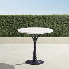 a white table sitting on top of a cement floor next to a green hedge covered wall