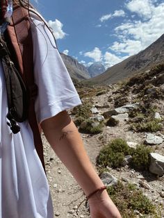 a person walking in the mountains with a backpack on their back and tattoos on their arm