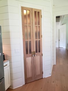 a kitchen with white walls and wood floors has an open door to the dining room