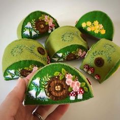 a hand is holding several green felt hats with flowers and mushrooms on them, all in different colors