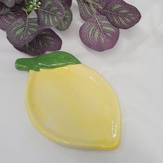 a yellow plate with a green leaf on it next to some purple flowers and leaves