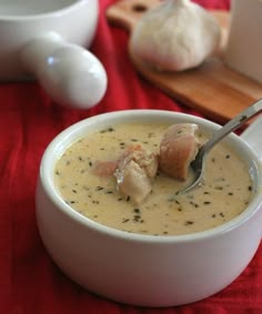 a white bowl filled with soup next to some garlic and other items on a red table cloth