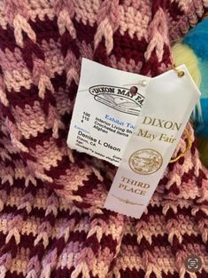 a close up of a knitted blanket with a label on it that says dixon may fair