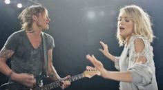 a man and woman are playing guitar in front of a microphone with their hands out