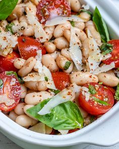 a white bowl filled with beans, tomatoes and spinach on top of a table