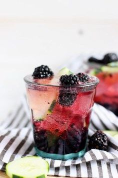 berries and cucumbers are garnished with minty water in glasses on a striped cloth