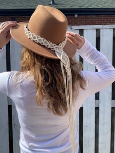 a woman with long hair wearing a brown hat and white shirt standing in front of a fence