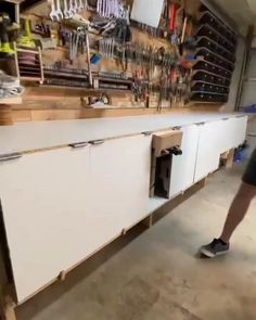 a man standing in front of a white cabinet with tools hanging on the wall behind it