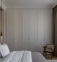 a white bed sitting in a bedroom next to a tall wooden headboard and wardrobes