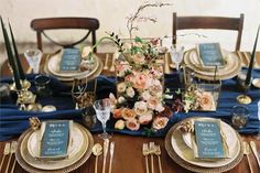 the table is set with gold and blue plates, silverware, and floral centerpieces