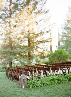 an outdoor ceremony with rows of chairs and flowers in the foreground, surrounded by tall trees