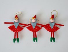 three red and green christmas ornaments with two elfs hanging from the top, one on each side