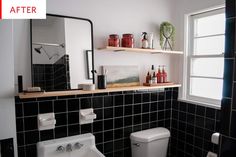 a bathroom with black tiles and white fixtures, including a mirror above the toilet bowl