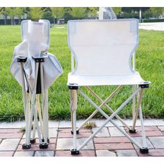 two white folding chairs sitting next to each other on a brick floor in the grass