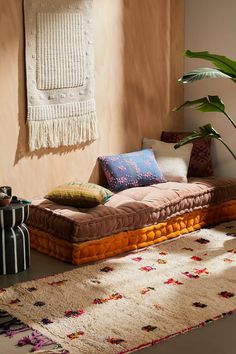 a living room filled with lots of furniture and pillows on top of a rug next to a potted plant