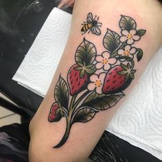 a strawberry and flower tattoo on the right arm, with a bee flying over it