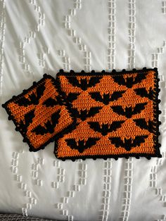 two orange and black place mats sitting on top of a white bed sheet with bats