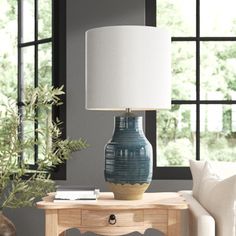 a table with a lamp on it in front of a couch and window sill