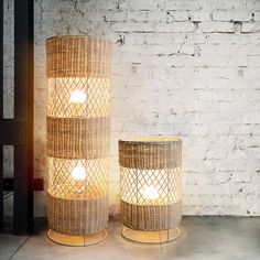 two wicker lamps sitting next to each other in front of a white brick wall