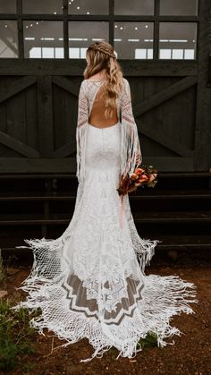 a woman in a white wedding dress standing on a dirt ground with her back to the camera