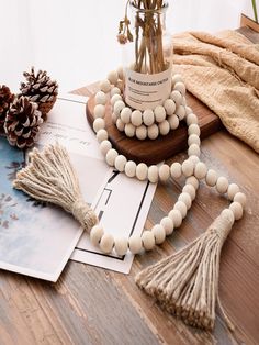 a wooden beaded necklace with tassels sits on a table next to pine cones