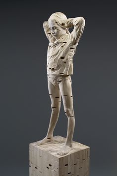 a sculpture of a man standing on top of a block of wood with his hands behind his head