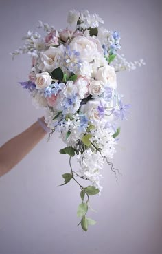 a bridal bouquet with white and blue flowers is being held by someone's hand